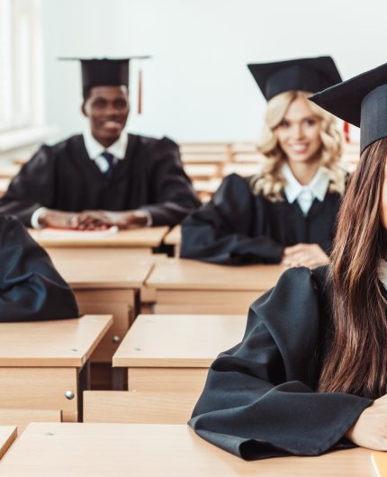 group of multiethnic students in graduation costumes sitting at class