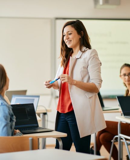 Happy IT teacher talking to her students during computer class at high school.