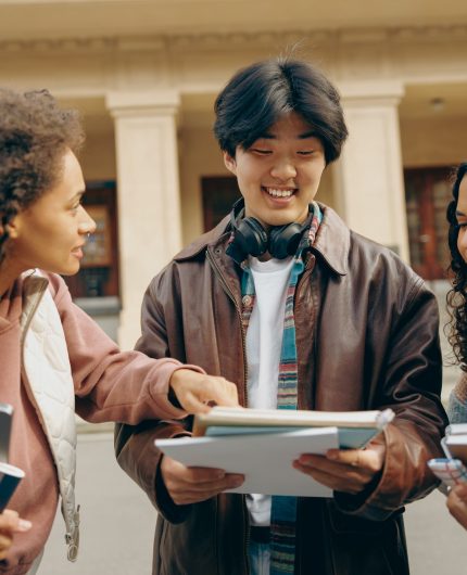 Happy students talking each other standing near university campus and holding books and laptop