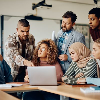 Multiracial group of college students and their teacher using computer in the classroom.