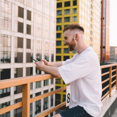 Smiling man using smartphone on terrace of building