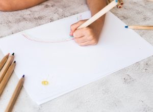 The child's hands are painted with colored pencils on a white paper.