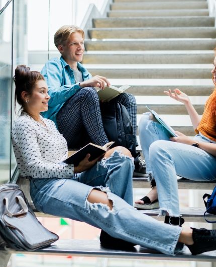 University students sitting on stairs and talking indoors, back to school concept